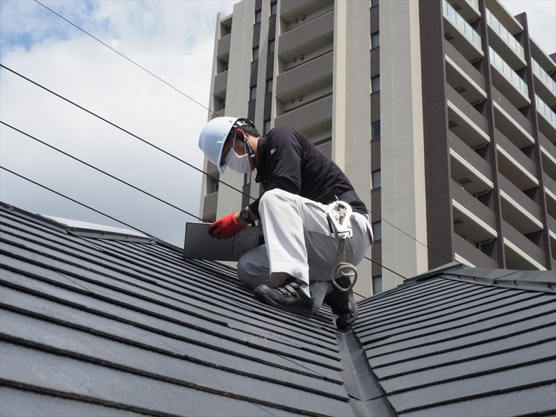 マンションを背に屋根で作業中の男性